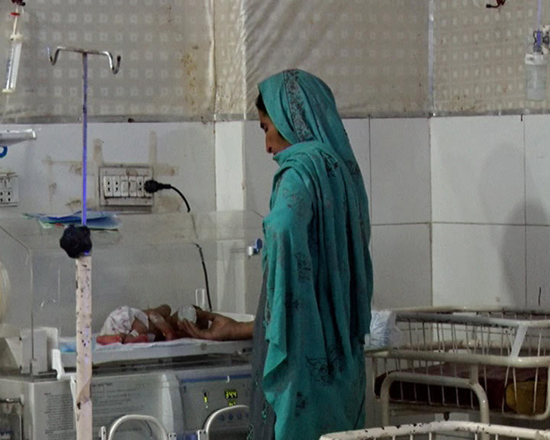 A grandmother stands at an incubator looking at her grandson lying in an incubator, looking worried about the health of the baby at Lady Reading Hospital in Peshawar, Pakistan. Photo by Wisal Yousafzai.
