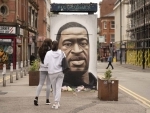 People gather by a mural of George Floyd in UK's Manchester