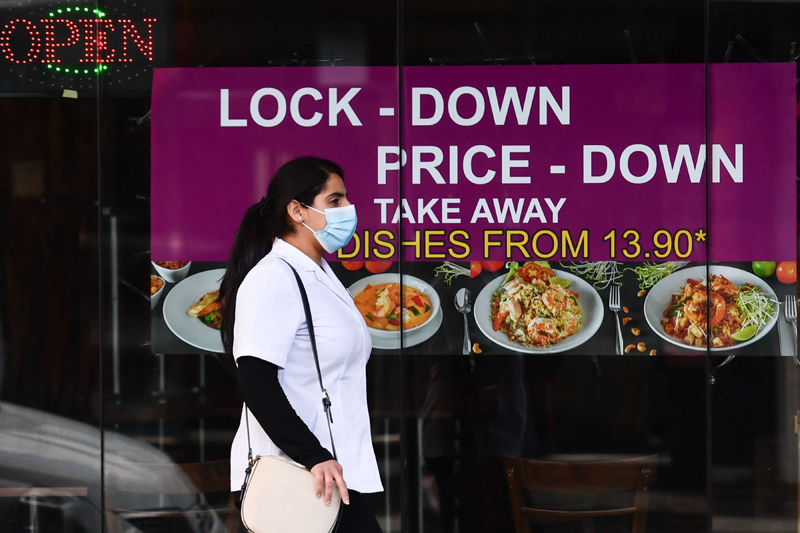 A woman wearing a face mask walks past a restaurant in Melbourne