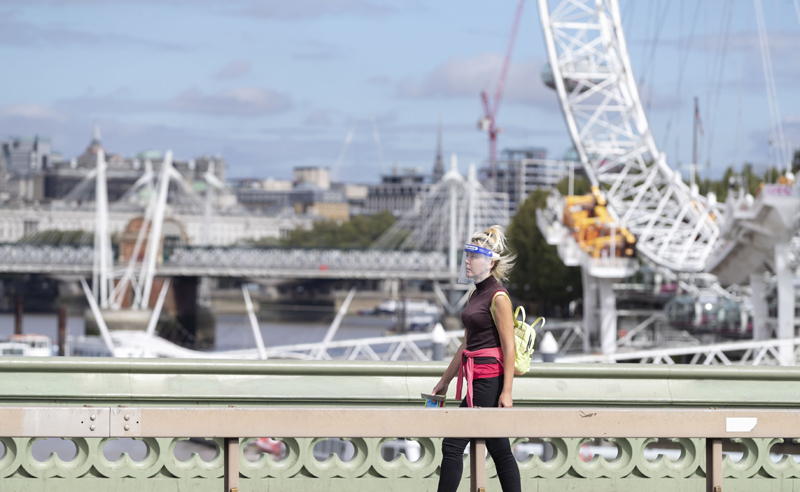 A woman wearing a face shield walks past the London Eye