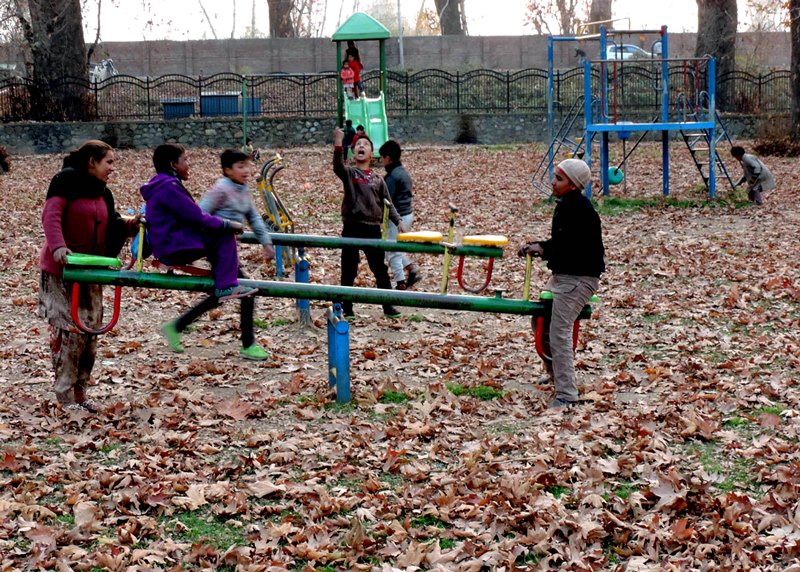 Children play in a park with Chinar leaves scattered all over in Kashmir